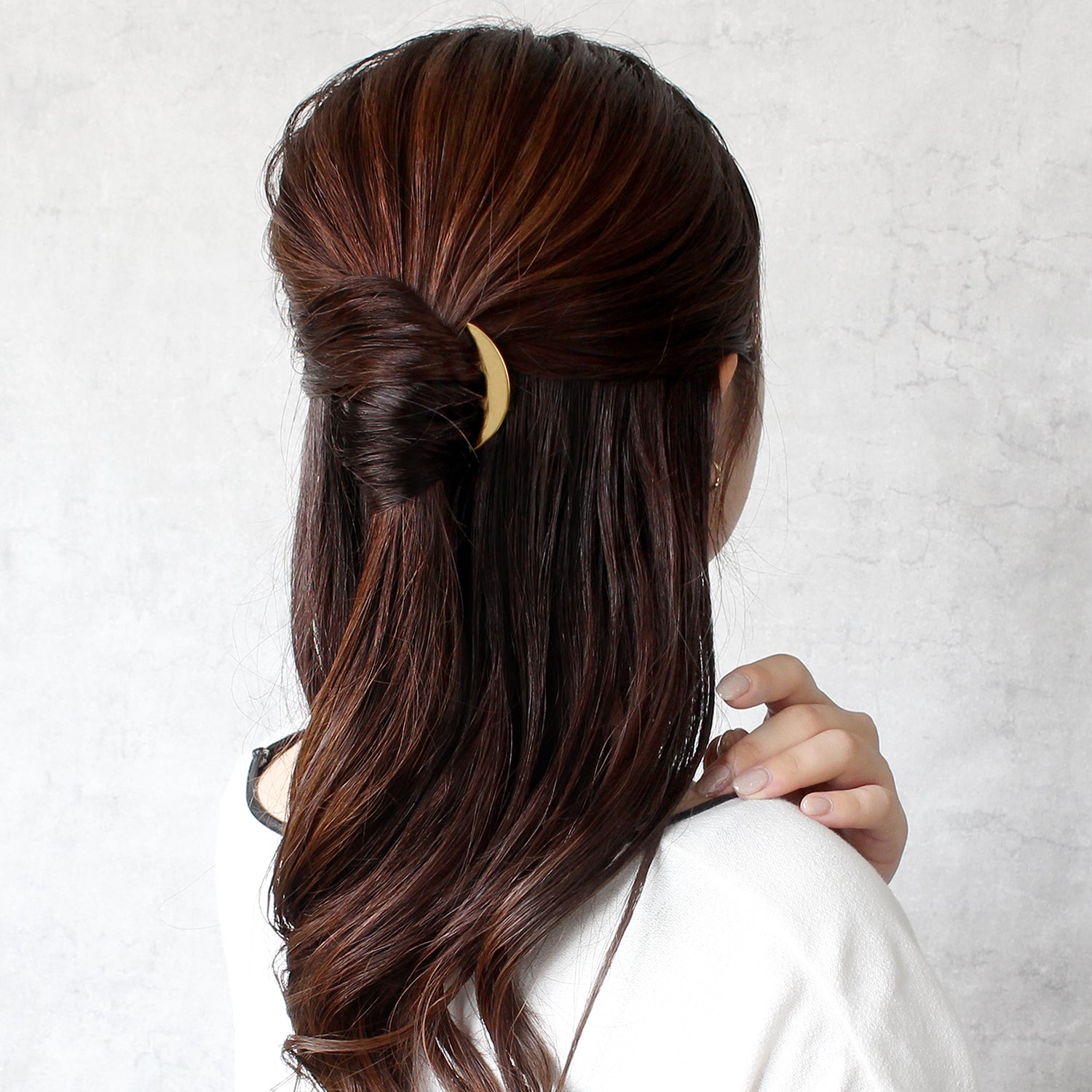 Woman with long brown hair styled in a half-up, half-down style wearing a kanzashi on a light gray background