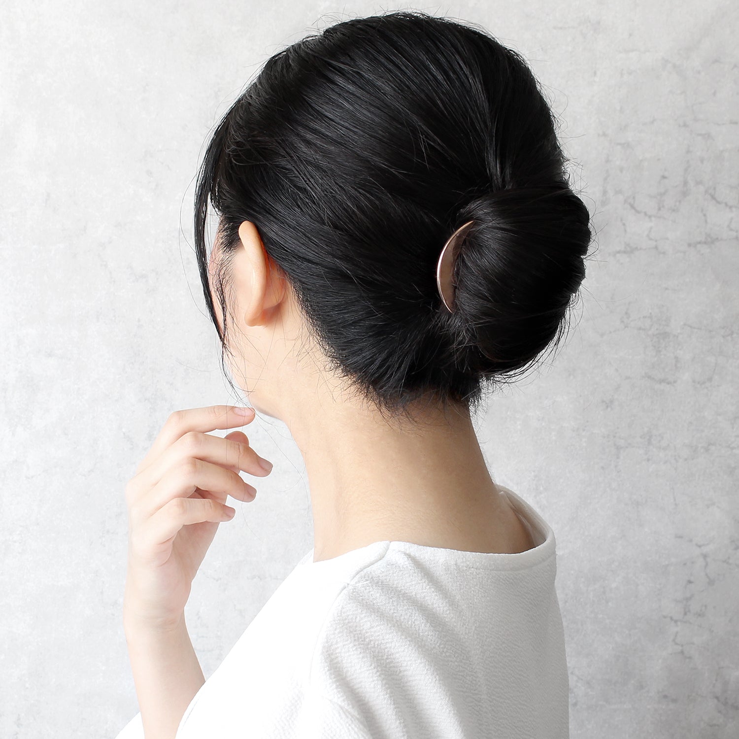 Person with a stylish hair bun wearing a white shirt against a light gray background with a rose gold kanzashi arc liner in her hair.